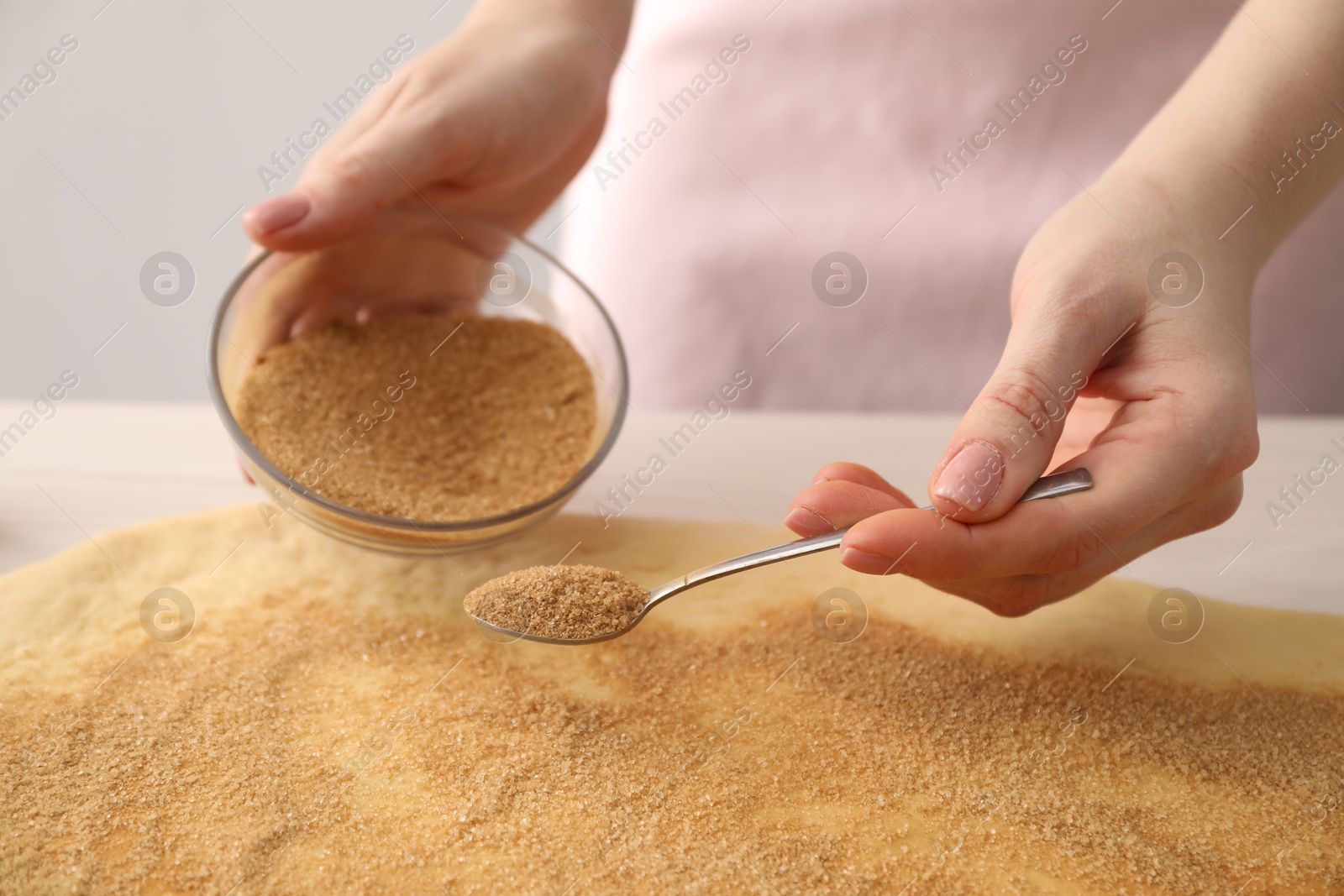 Photo of Making cinnamon rolls. Woman adding spice with sugar into dough at table, closeup