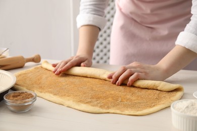 Photo of Making cinnamon rolls. Woman shaping dough at white wooden table, closeup