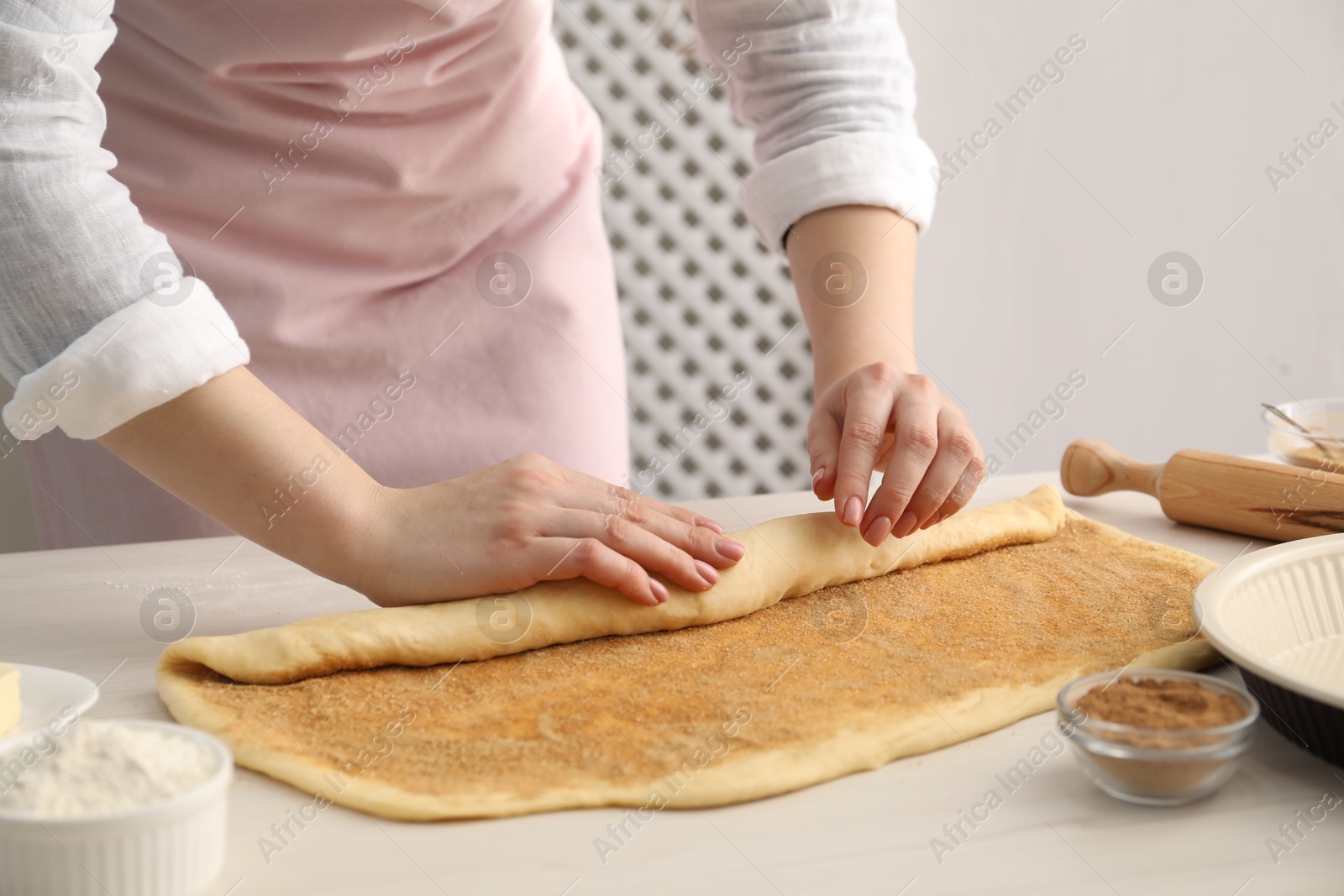 Photo of Making cinnamon rolls. Woman shaping dough at white wooden table, closeup