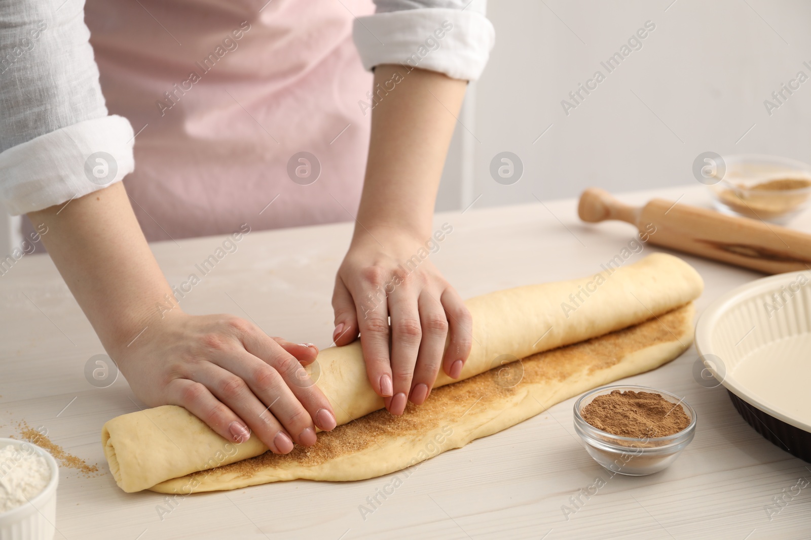 Photo of Making cinnamon rolls. Woman shaping dough at white wooden table, closeup