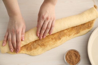 Photo of Making cinnamon rolls. Woman shaping dough at white wooden table, top view