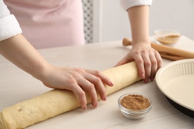 Photo of Making cinnamon rolls. Woman shaping dough at white wooden table, closeup