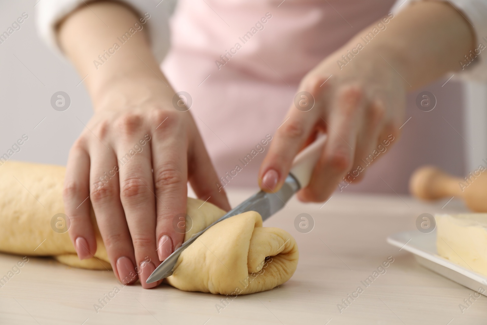 Photo of Making cinnamon rolls. Woman cutting dough at white wooden table, closeup