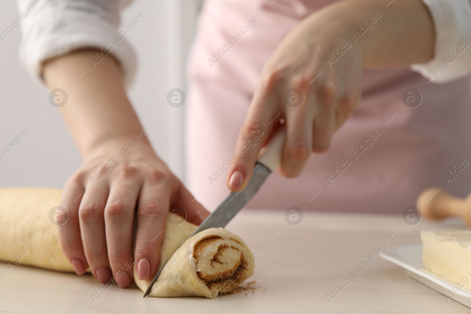 Photo of Making cinnamon rolls. Woman cutting dough at white wooden table, closeup