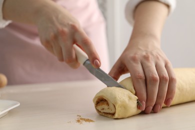 Photo of Making cinnamon rolls. Woman cutting dough at white wooden table, closeup