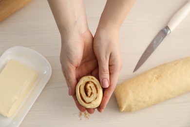 Photo of Woman with uncooked cinnamon roll at white wooden table, top view