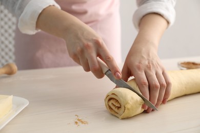 Photo of Making cinnamon rolls. Woman cutting dough at white wooden table, closeup