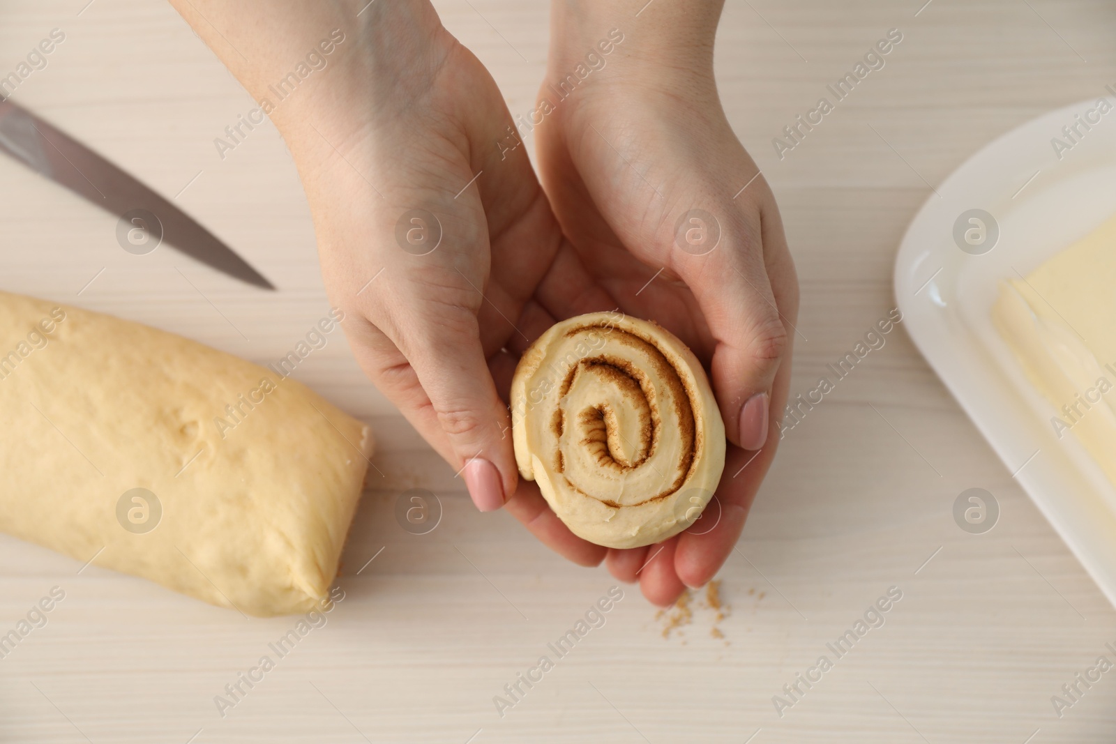 Photo of Woman with uncooked cinnamon roll at white wooden table, top view