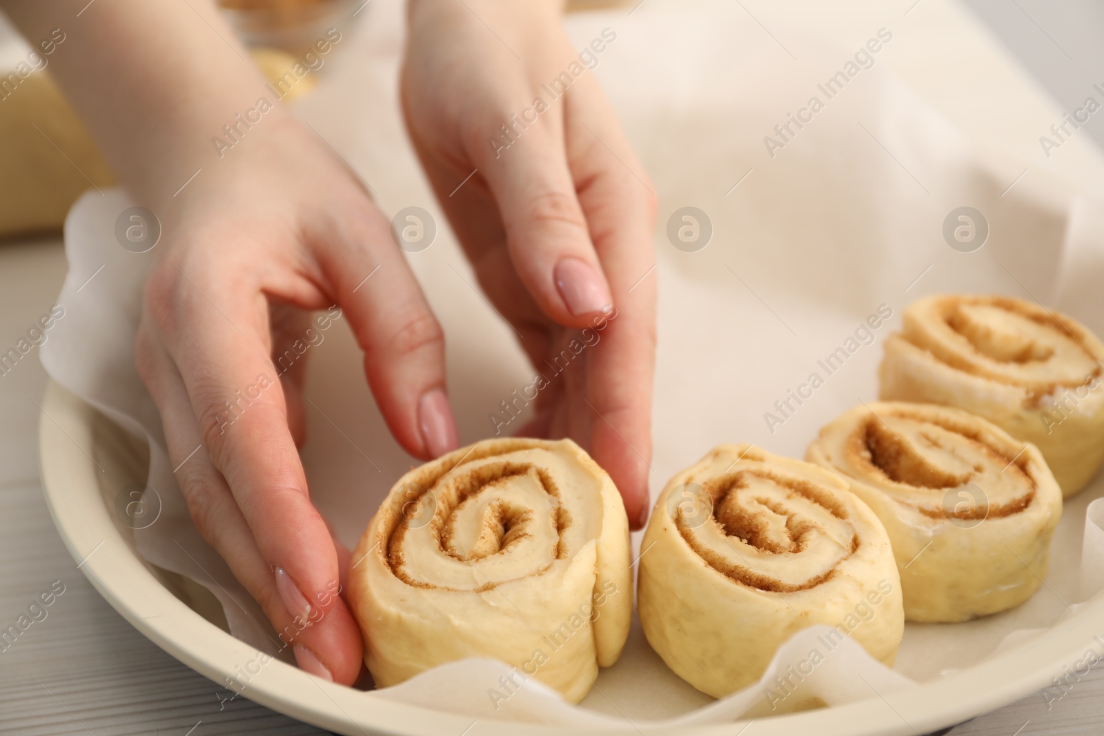 Photo of Woman putting cinnamon roll into baking dish at table, closeup