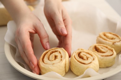 Photo of Woman putting cinnamon roll into baking dish at table, closeup