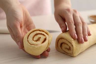 Photo of Woman making cinnamon rolls at white wooden table, closeup