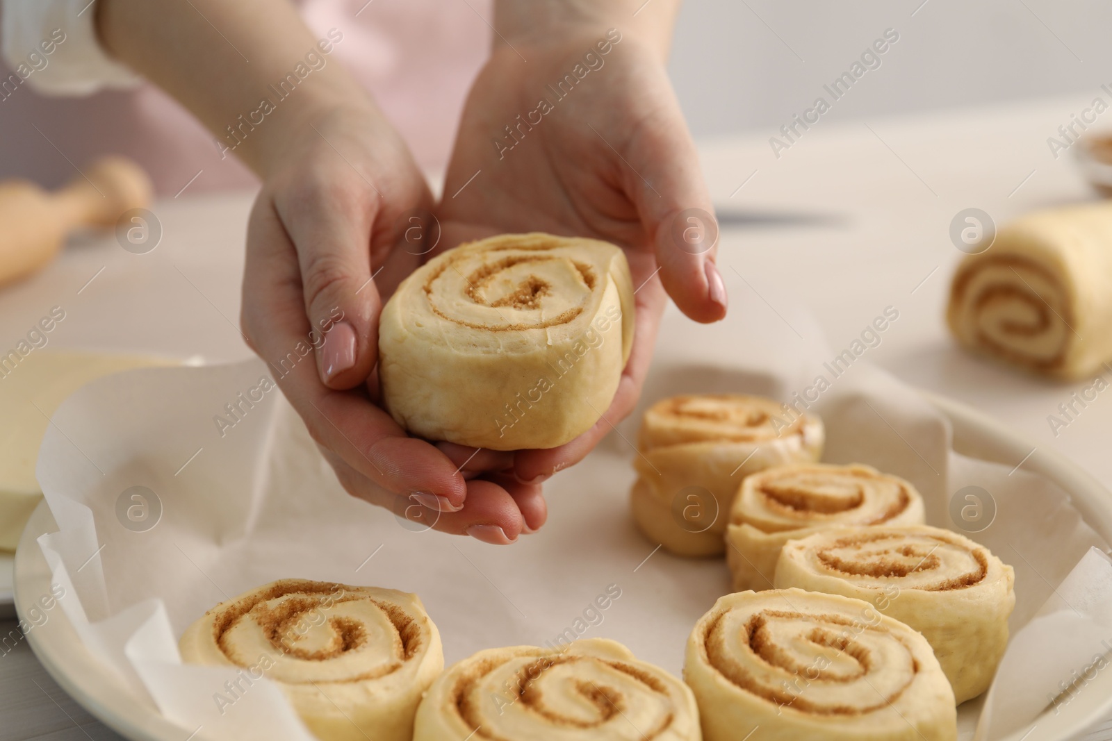 Photo of Woman putting cinnamon roll into baking dish at table, closeup