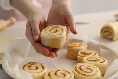 Photo of Woman putting cinnamon roll into baking dish at table, closeup