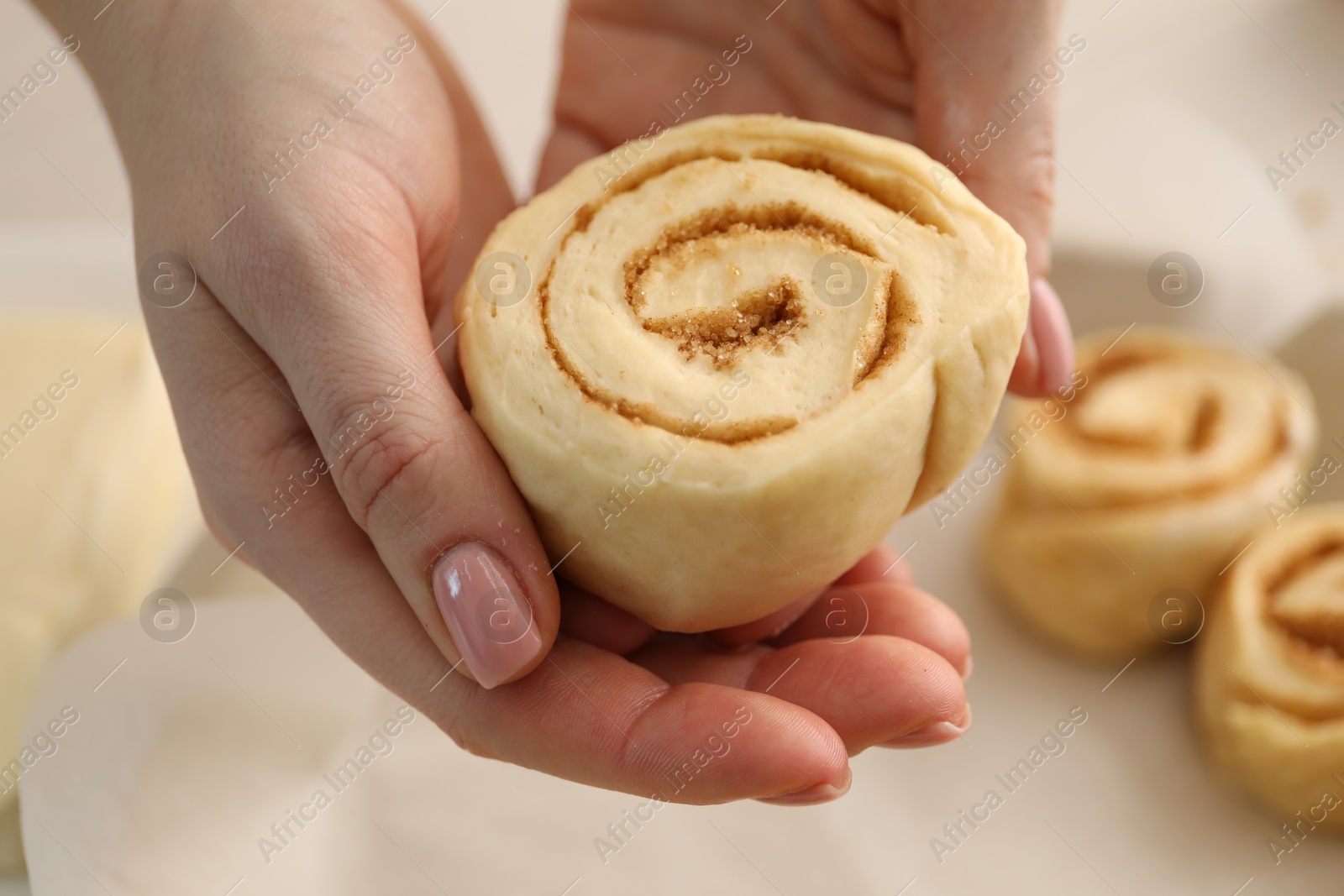 Photo of Woman with uncooked cinnamon roll at table, closeup