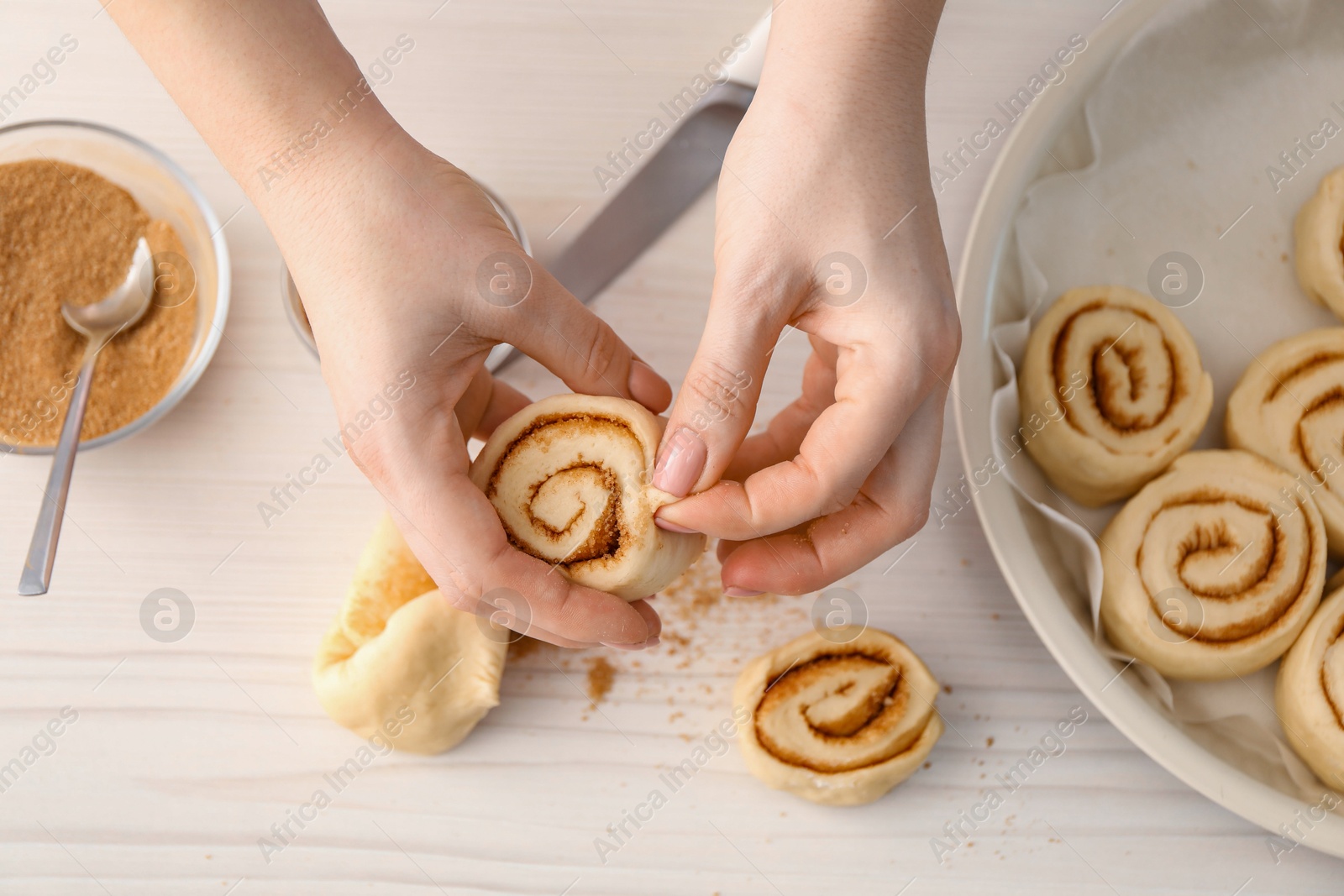 Photo of Woman making cinnamon rolls at white wooden table, top view