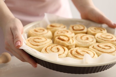 Woman holding baking dish with uncooked cinnamon rolls at table, closeup