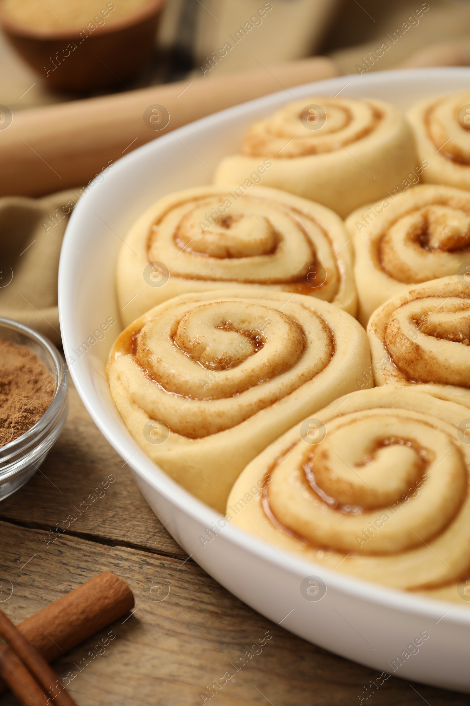 Photo of Raw cinnamon rolls in baking dish on wooden table, closeup