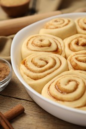 Photo of Raw cinnamon rolls in baking dish on wooden table, closeup