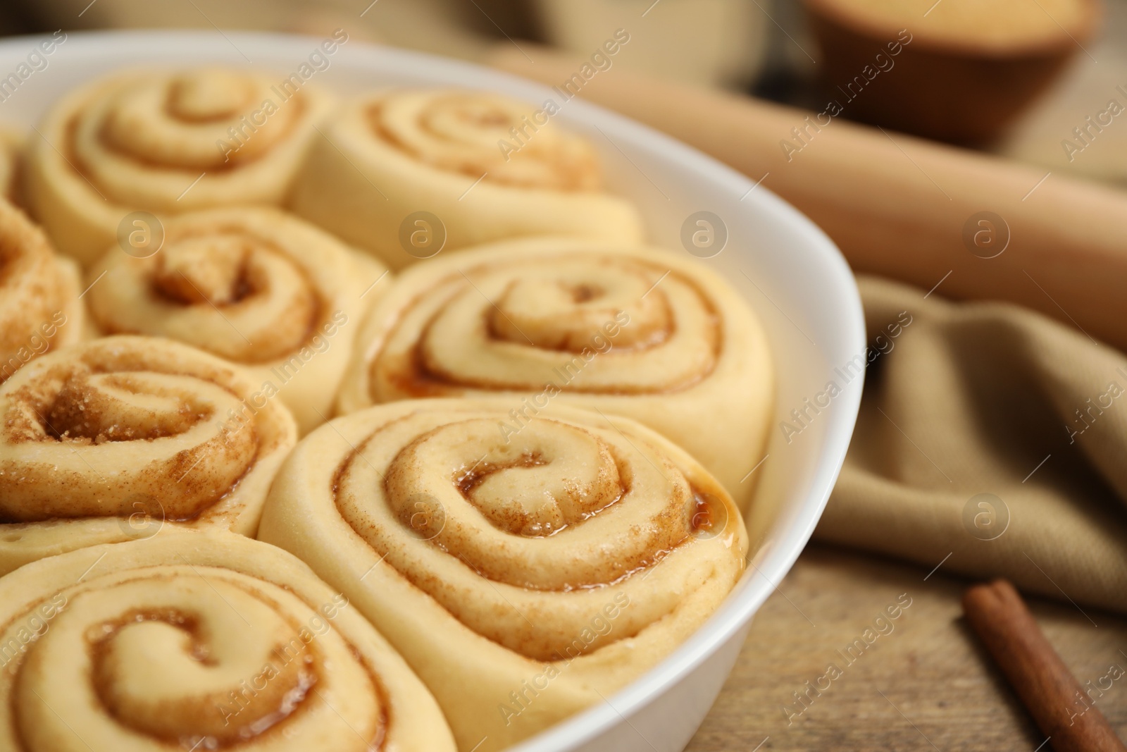 Photo of Raw cinnamon rolls in baking dish on table, closeup