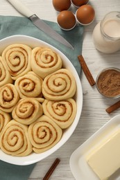 Photo of Raw cinnamon rolls and different ingredients on light wooden table, flat lay