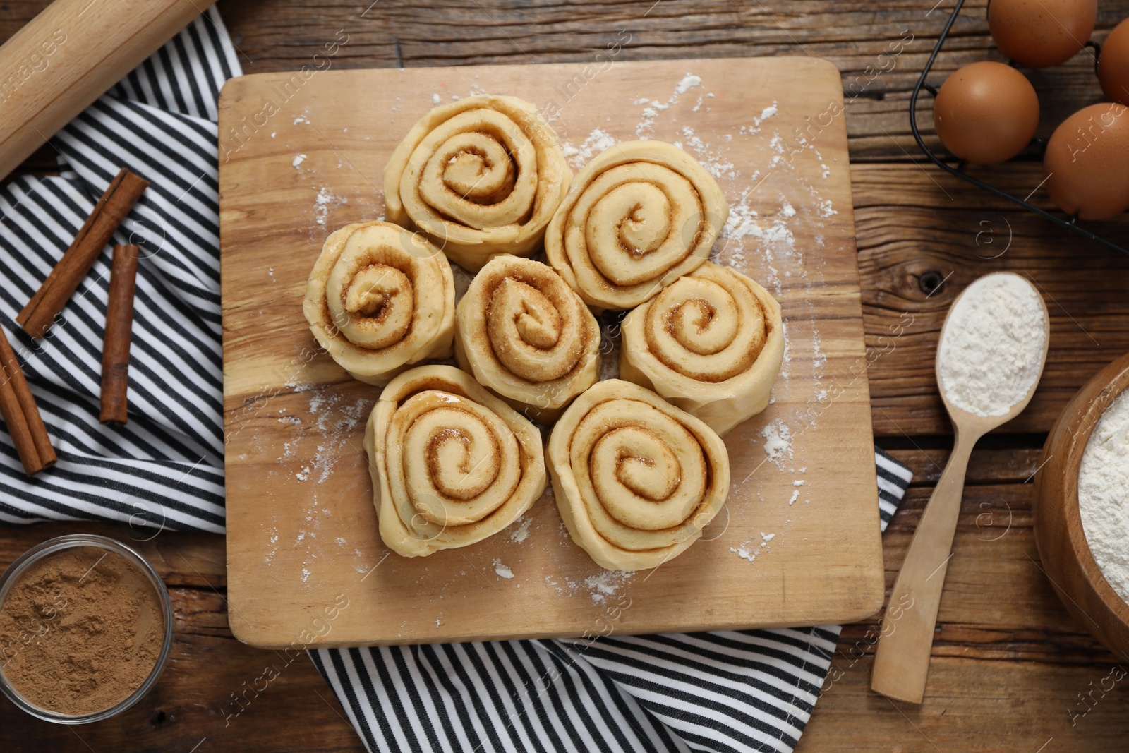 Photo of Raw cinnamon rolls and different ingredients on wooden table, flat lay