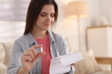 Photo of Woman with pill reading instruction at home, selective focus