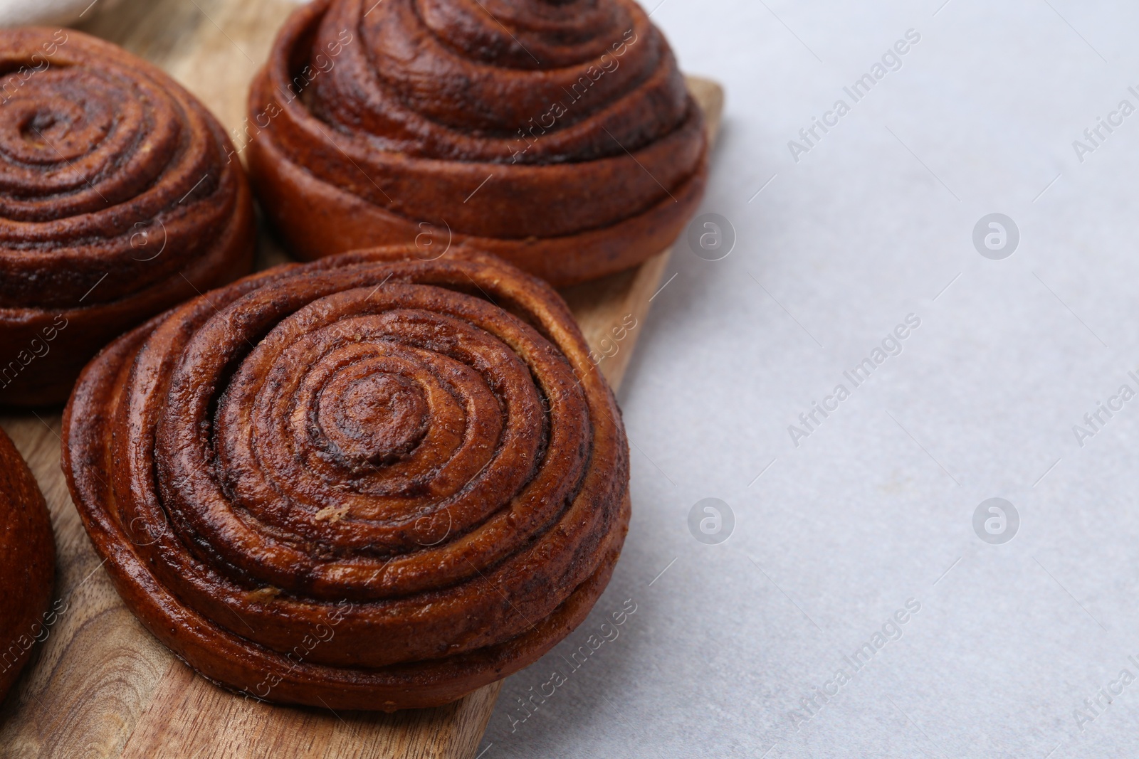 Photo of Delicious cinnamon roll buns on light table, closeup. Space for text