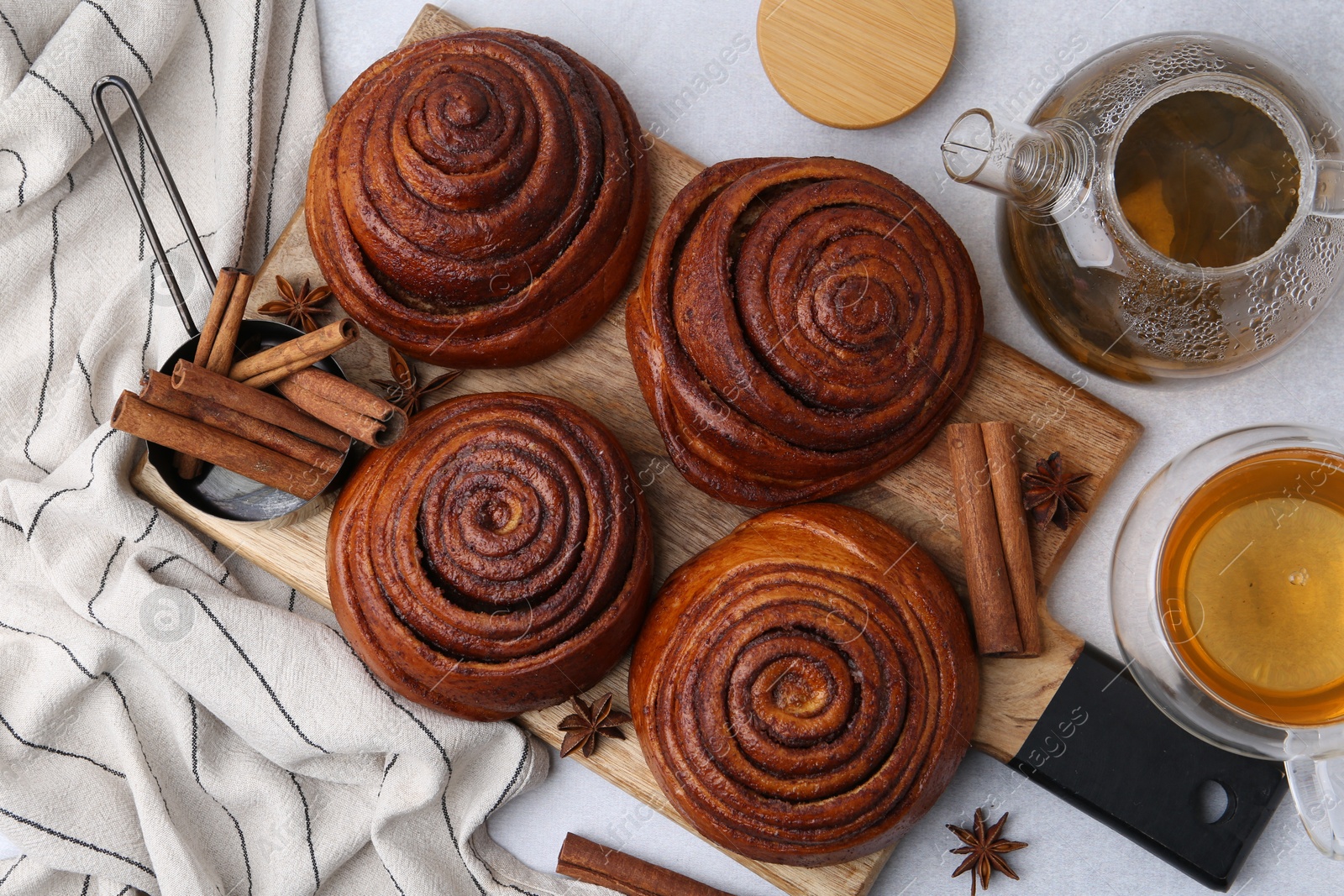 Photo of Delicious cinnamon roll buns and tea on light table, flat lay