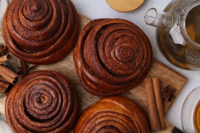 Photo of Delicious cinnamon roll buns and tea on light table, flat lay