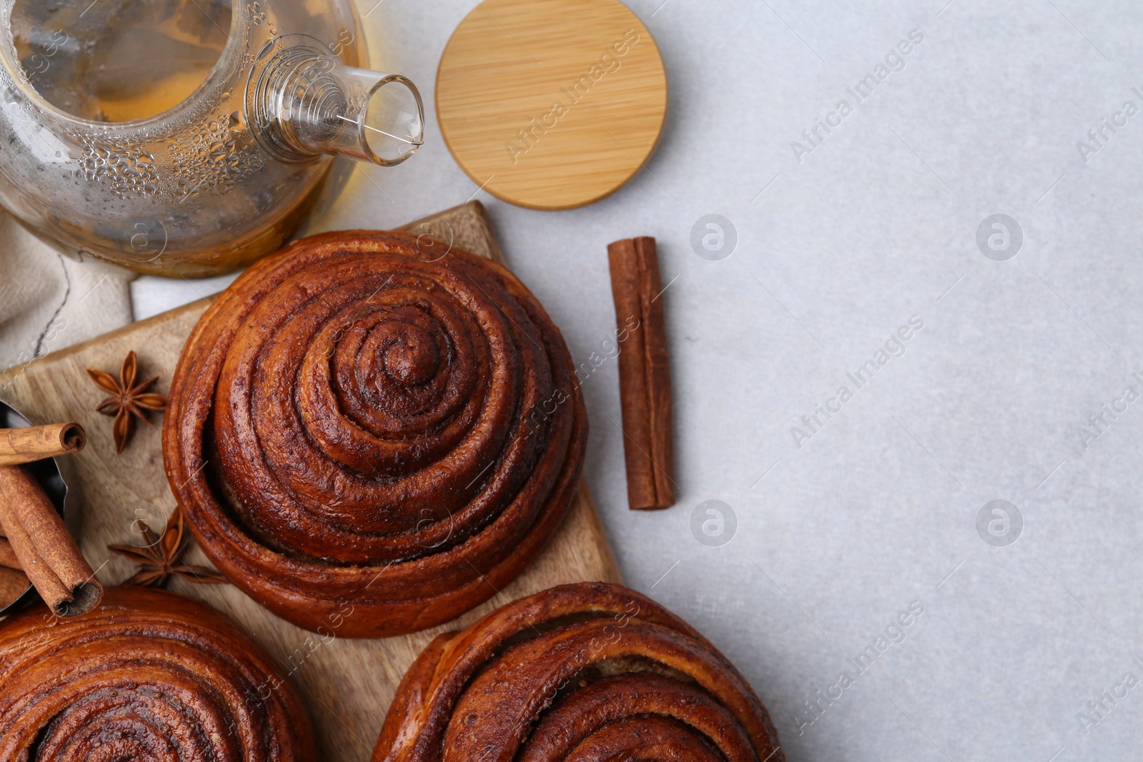 Photo of Delicious cinnamon roll buns and tea on light table, flat lay. Space for text