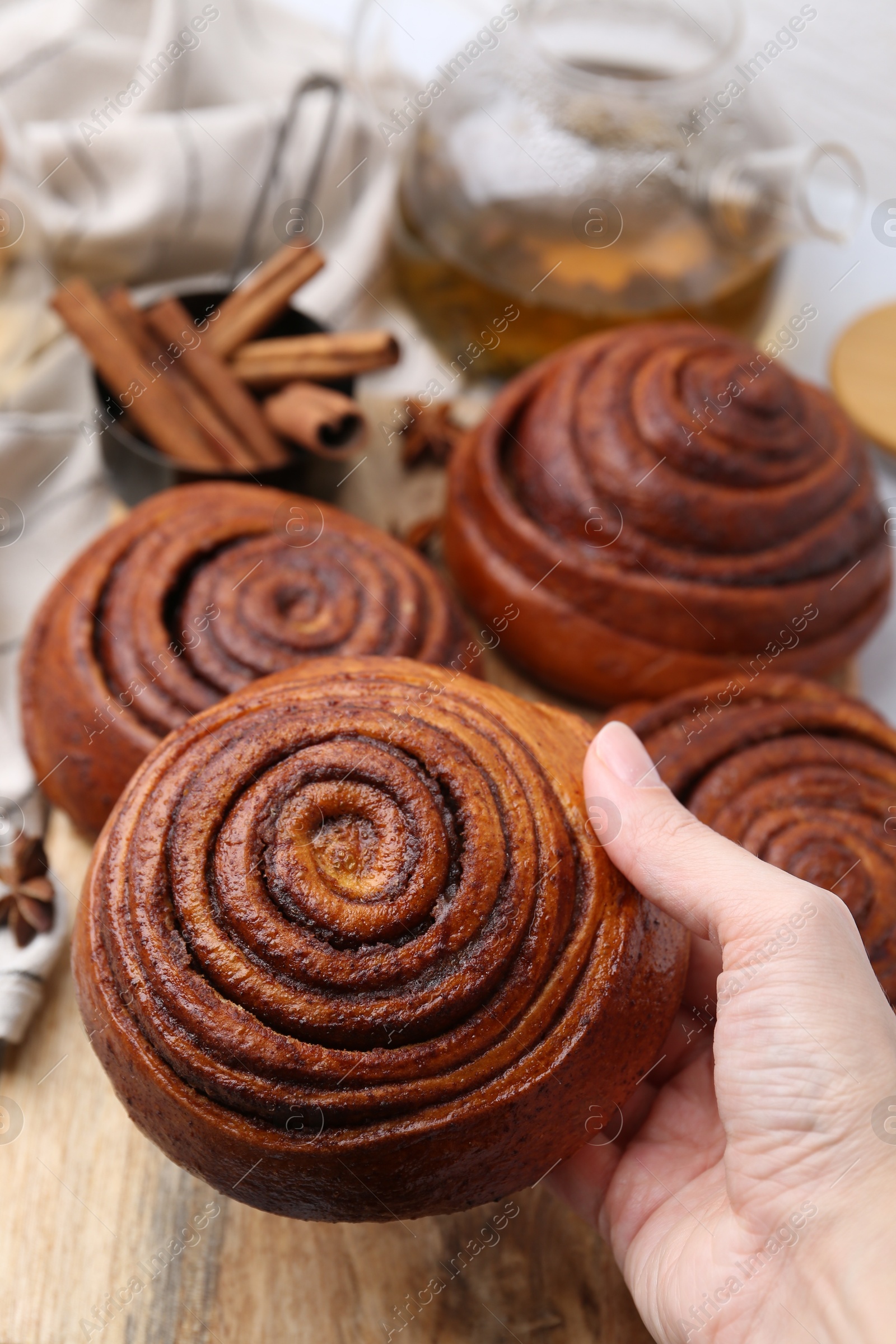 Photo of Woman with delicious cinnamon roll buns at table, closeup