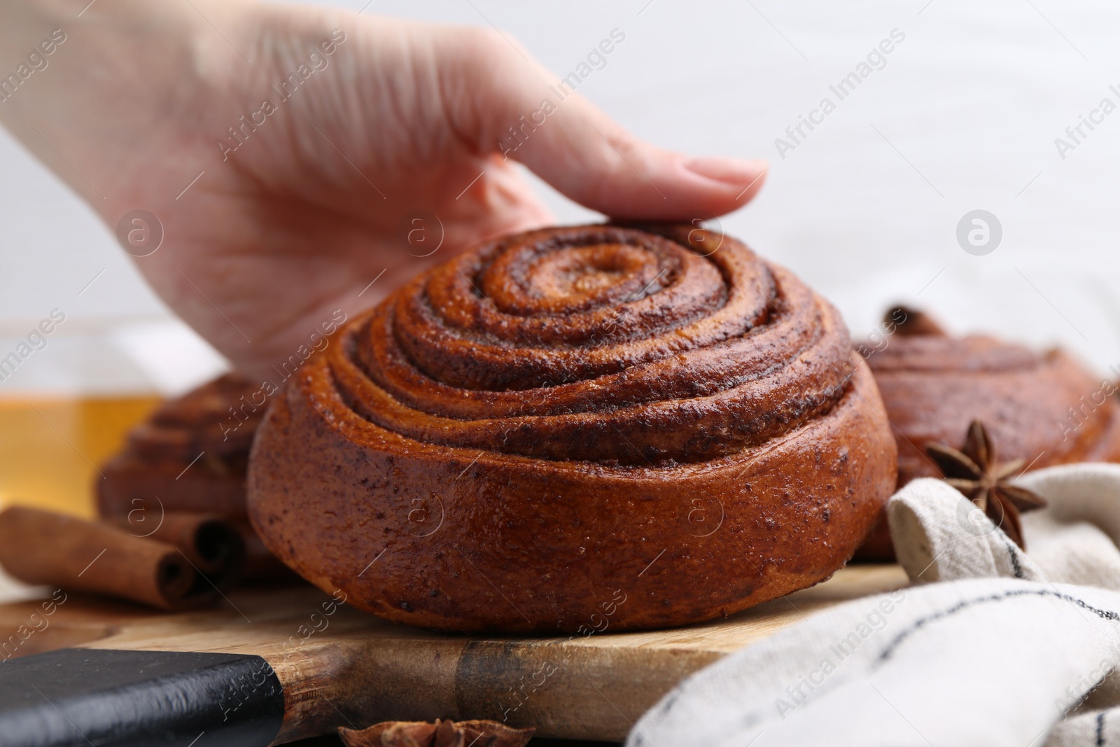 Photo of Woman with delicious cinnamon roll bun at table, closeup