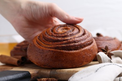 Photo of Woman with delicious cinnamon roll bun at table, closeup