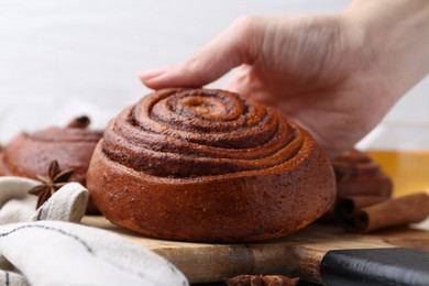 Photo of Woman with delicious cinnamon roll bun at table, closeup