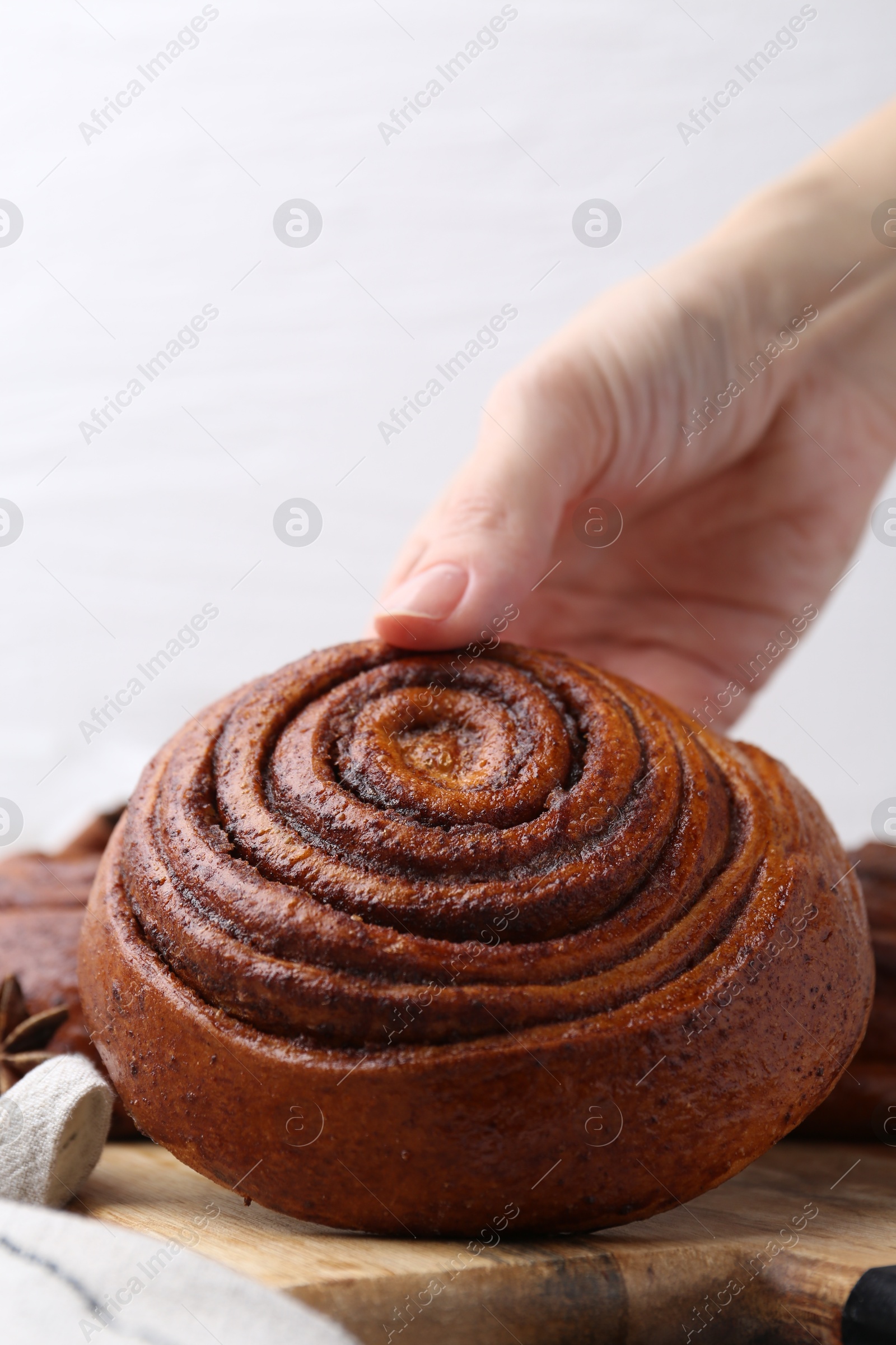 Photo of Woman with delicious cinnamon roll bun at table, closeup