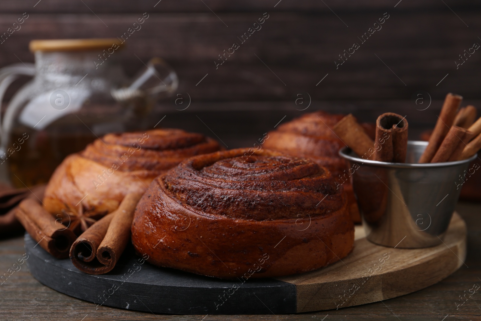 Photo of Delicious cinnamon roll buns and spices on wooden table, closeup