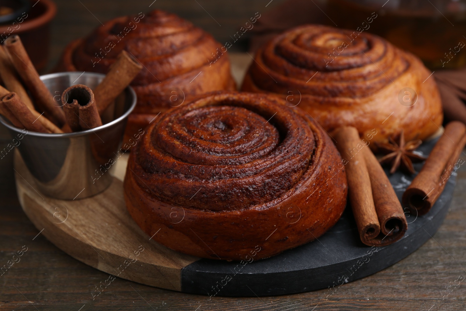 Photo of Delicious cinnamon roll buns and spices on wooden table, closeup