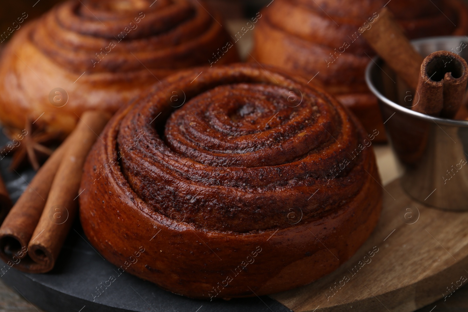 Photo of Delicious cinnamon roll buns and spices on wooden table, closeup