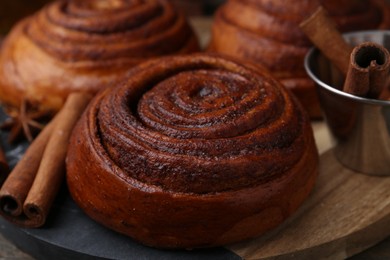 Photo of Delicious cinnamon roll buns and spices on wooden table, closeup