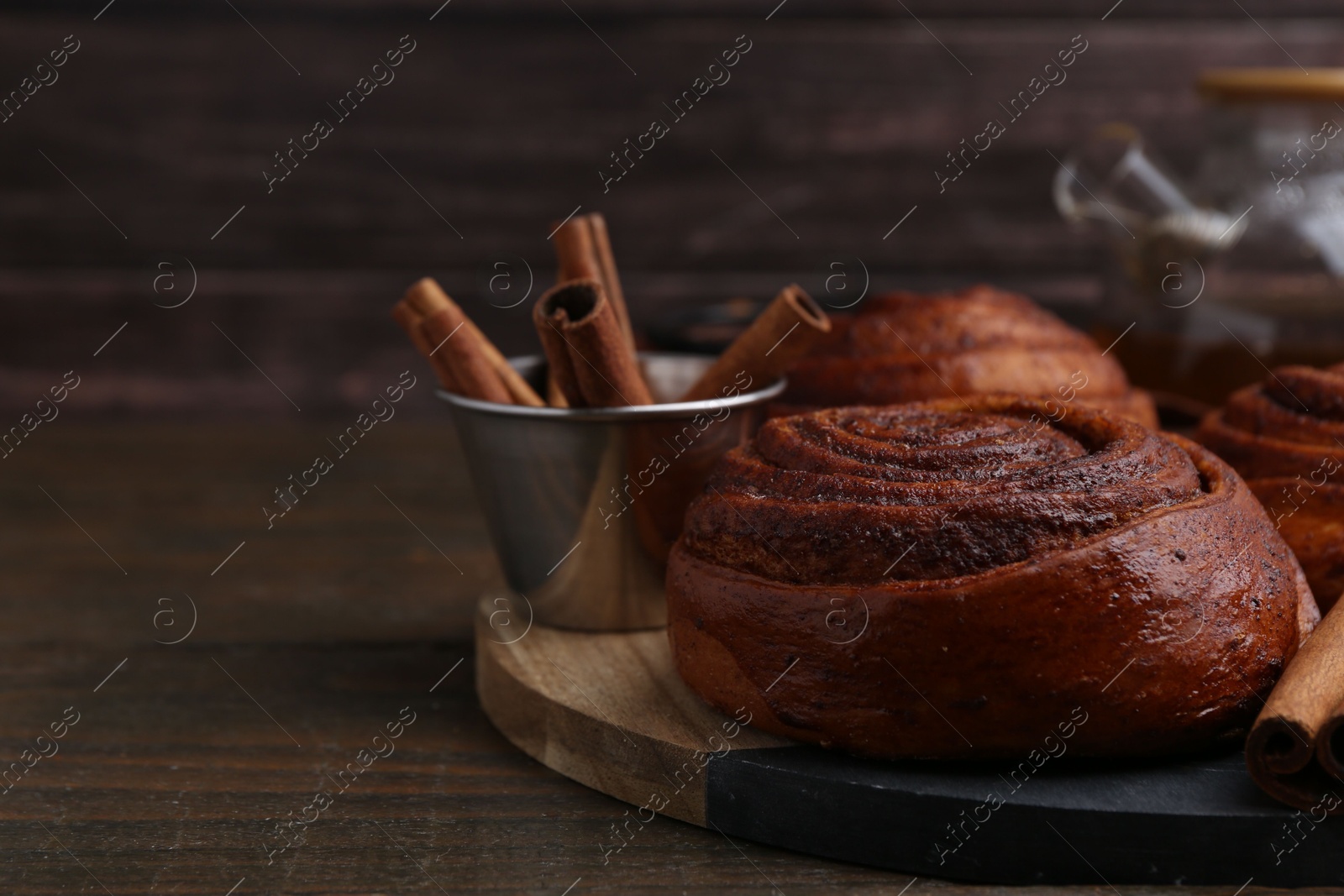 Photo of Delicious cinnamon roll buns and spices on wooden table, closeup