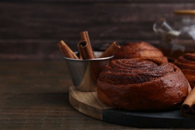 Photo of Delicious cinnamon roll buns and spices on wooden table, closeup