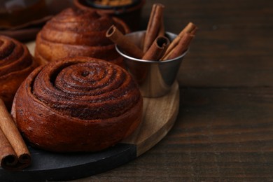 Photo of Delicious cinnamon roll buns and spices on wooden table, closeup