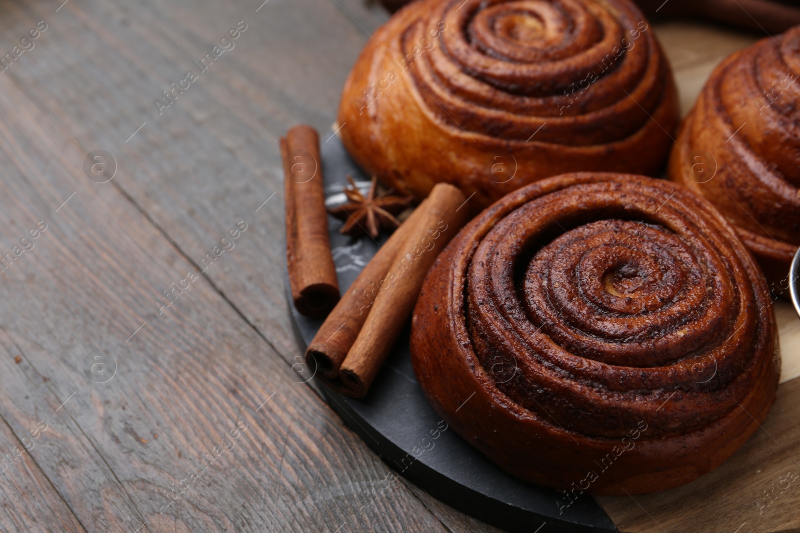 Photo of Delicious cinnamon roll buns and spices on wooden table, closeup. Space for text