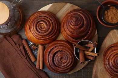 Photo of Delicious cinnamon roll buns and spices on wooden table, flat lay