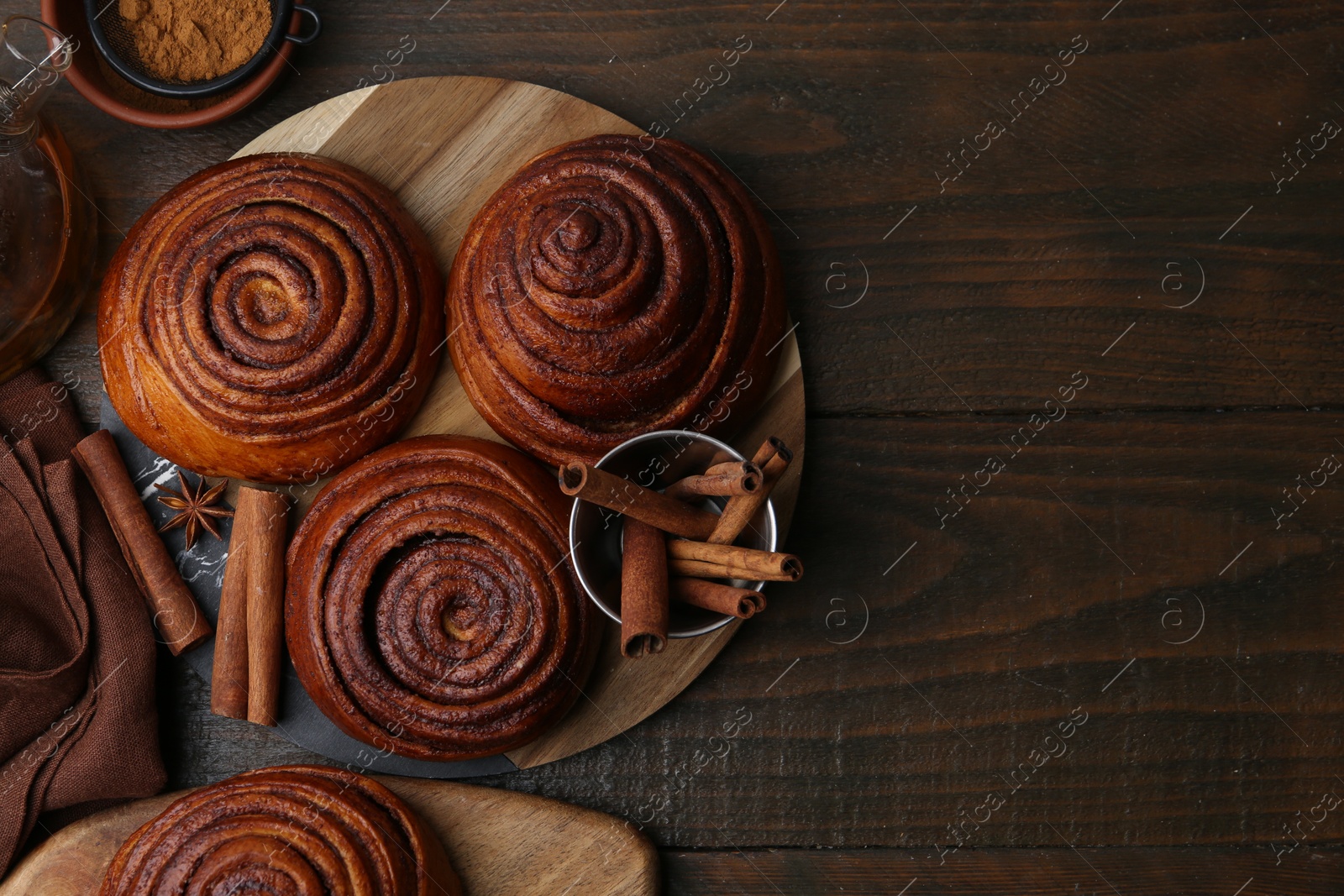 Photo of Delicious cinnamon roll buns and spices on wooden table, flat lay. Space for text