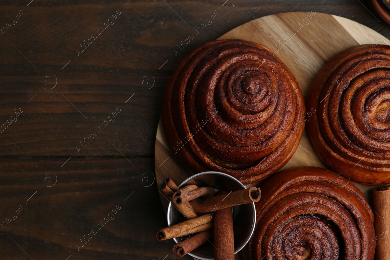 Photo of Delicious cinnamon roll buns on wooden table, top view. Space for text