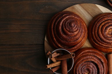 Photo of Delicious cinnamon roll buns on wooden table, top view. Space for text