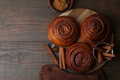 Photo of Delicious cinnamon roll buns and spices on wooden table, flat lay. Space for text