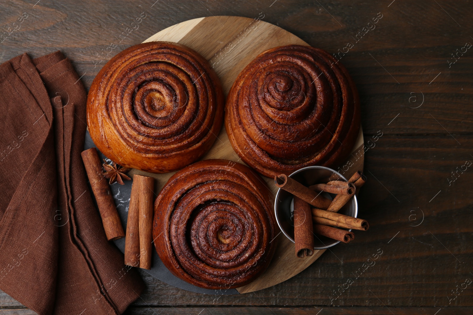 Photo of Delicious cinnamon roll buns and spices on wooden table, top view