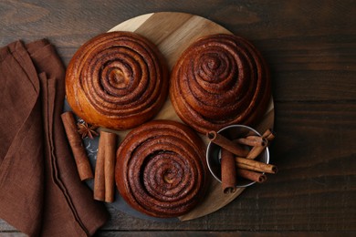 Photo of Delicious cinnamon roll buns and spices on wooden table, top view